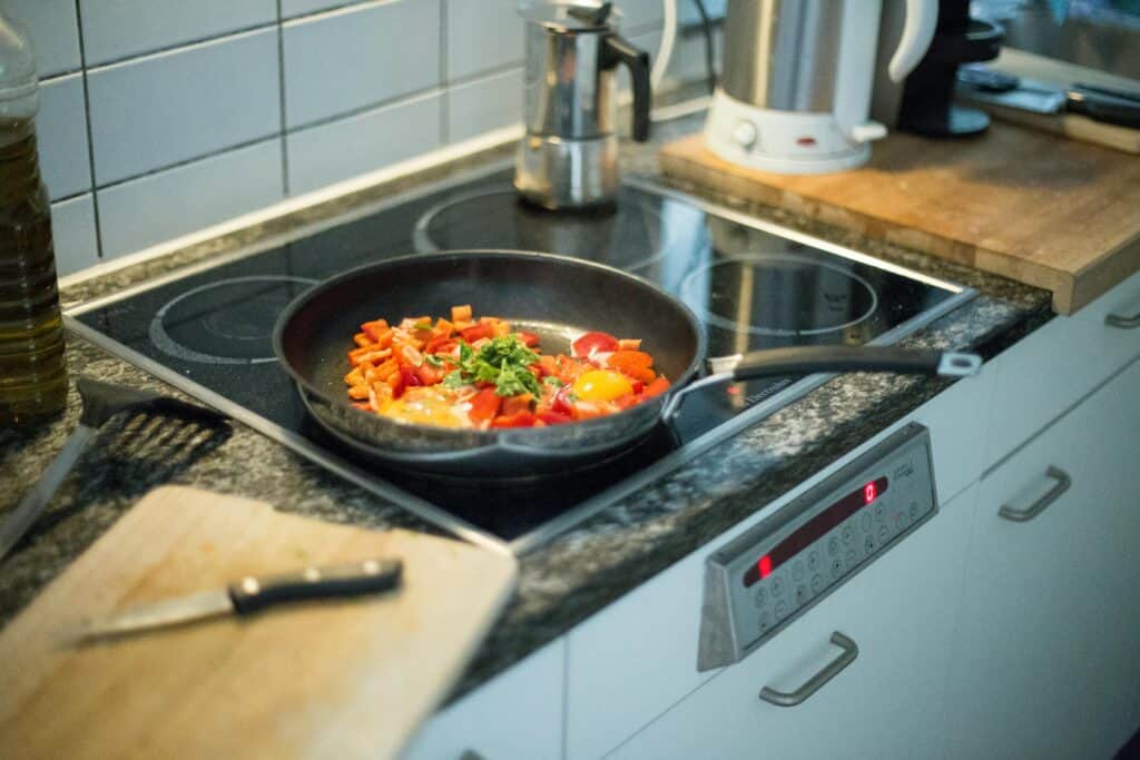 A colorful pan with eggs and vegetables cooking on an electric stove in a modern kitchen setting.